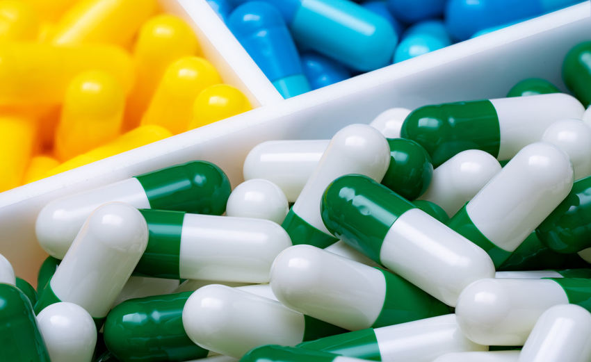 Selective focus on green-white capsule pills in plastic box on blue and yellow capsule pills. 