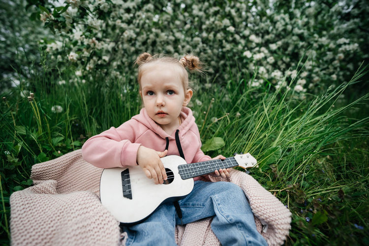 Little girl playing the ukulele in a blooming apple orchard in nature
