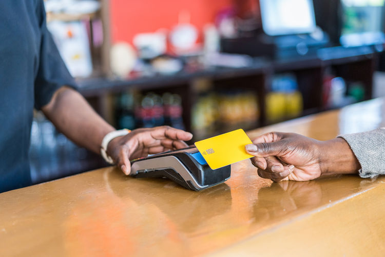 Crop unrecognizable customer making payment with plastic card on pos terminal at counter in bar person