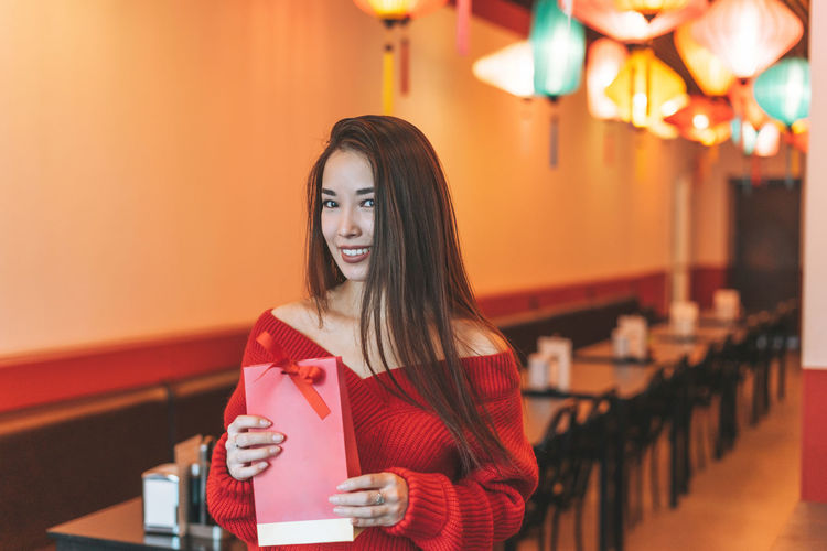 Beautiful young asian woman in red clothes with red gift bag celebrating chinese new year