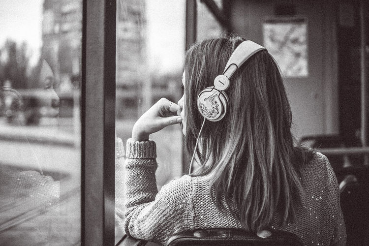 Thoughtful woman wearing headphones while sitting in bus