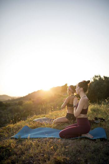 Women practicing yoga on mats against clear sky at sunset