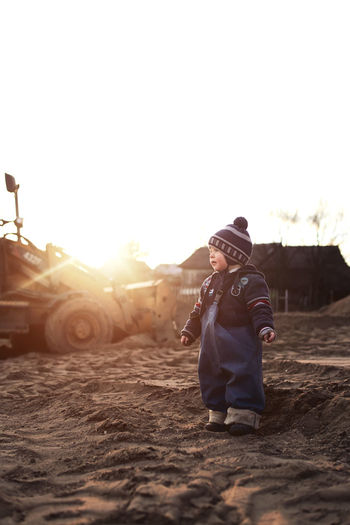 A boy in the village on the background of a tractor walks on the sand .