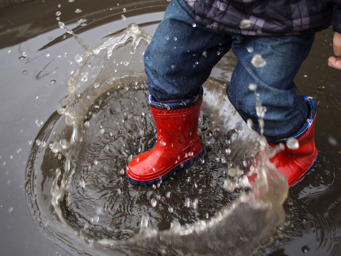 Low section of child wearing rubber boots jumping in puddle during monsoon