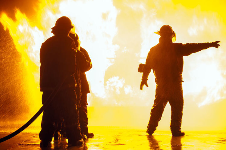 Silhouette firefighters spraying water on fire at night