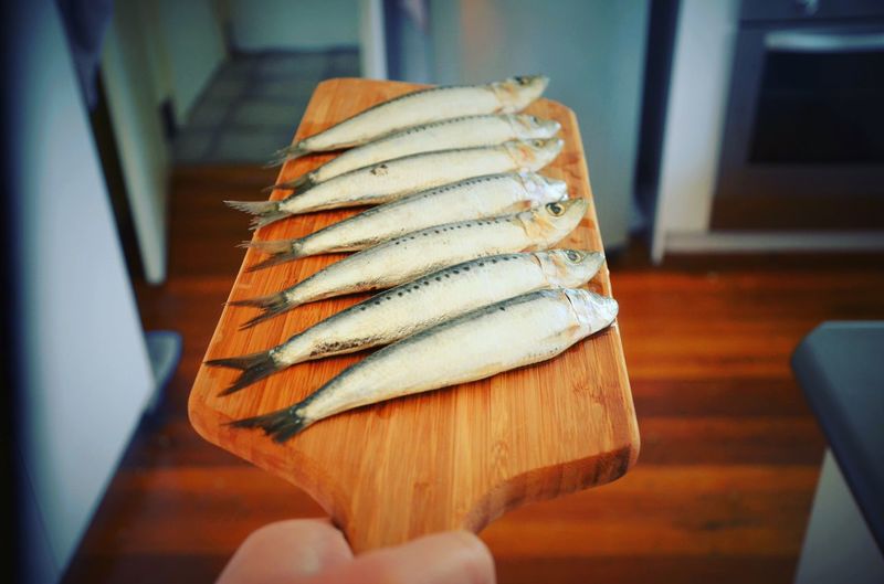 Cropped image of hand holding sardines in wooden tray at home
