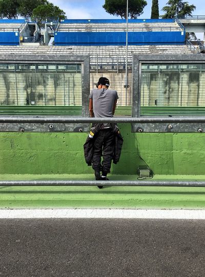Full length rear view of man standing by motor racing track on sunny day