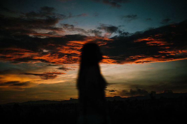 Silhouette woman standing on field against cloudy sky during sunset