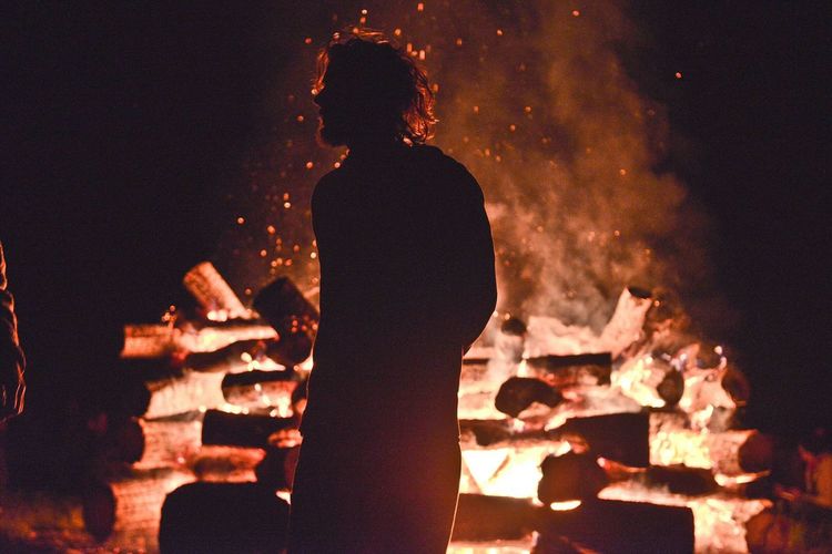 Man standing by bonfire on field at night