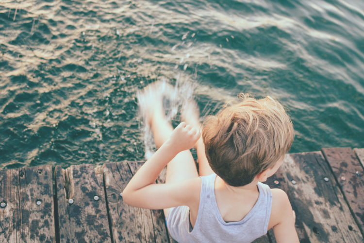 High angle view of boy having fun while splashing water on a pier.