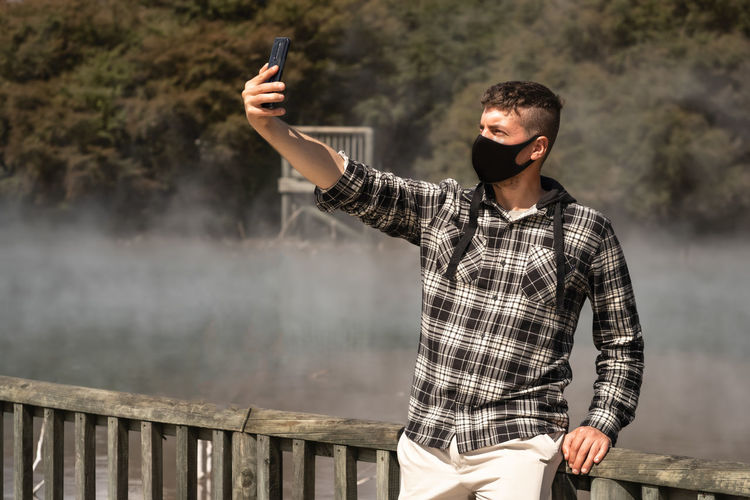Man wearing mask taking selfie while standing by railing