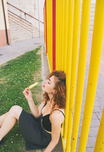 High angle view of woman having popsicle while sitting by yellow railing