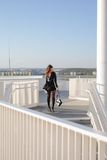 Woman walking on footbridge against clear sky