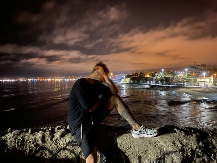 Young man standing at beach against sky at night