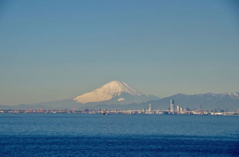 Scenic view of ocean and mountains against clear blue sky