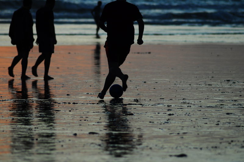 Silhouette man playing soccer at beach during sunset