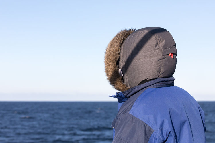 Rear view of person wearing hooded shirt at norwegian sea against clear sky