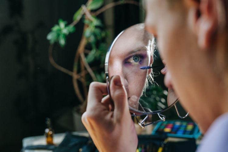 Reflection of man applying mascara in hand mirror