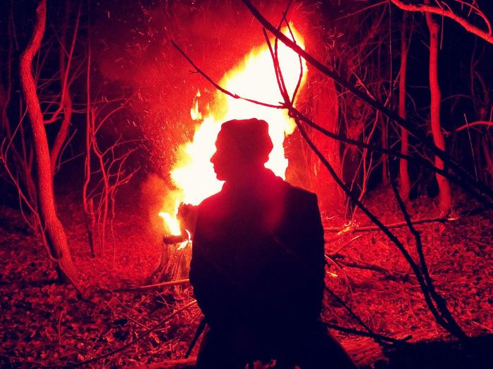 Silhouette of man sitting by bonfire at night