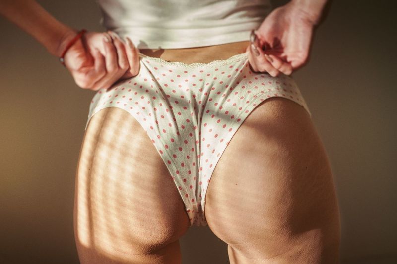 Midsection of woman wearing panties while standing against wall