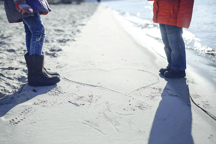 Low section of couple standing by heart shape at beach