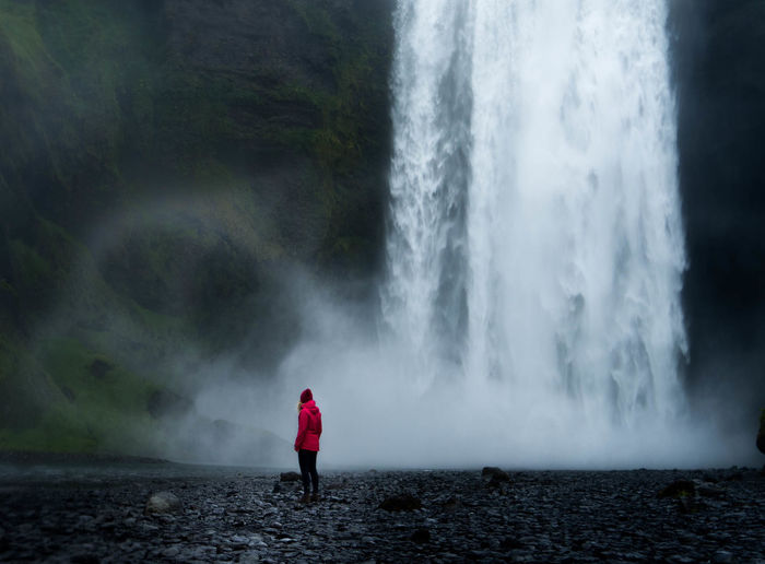 Side view of mid adult woman standing against waterfall