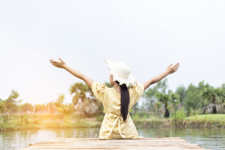 Rear view of woman with arms raised in lake against sky
