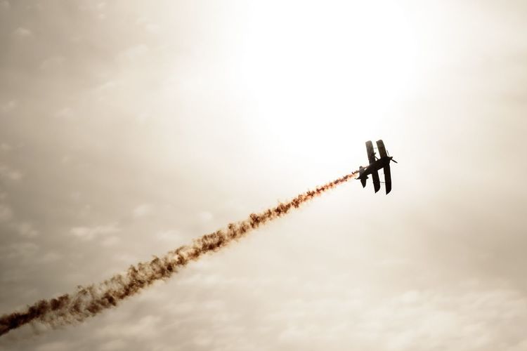 Low angle view of silhouette aerobatic biplane with vapor trail against sky