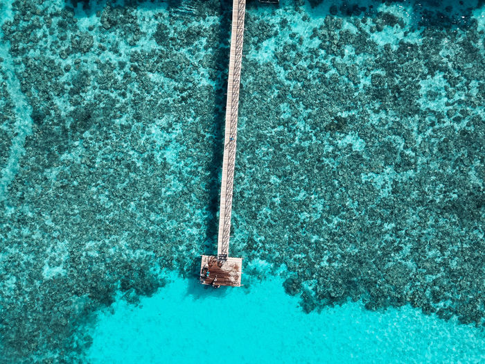 Top down aerial view over the end of wooden jetty with unidentified kids on it.