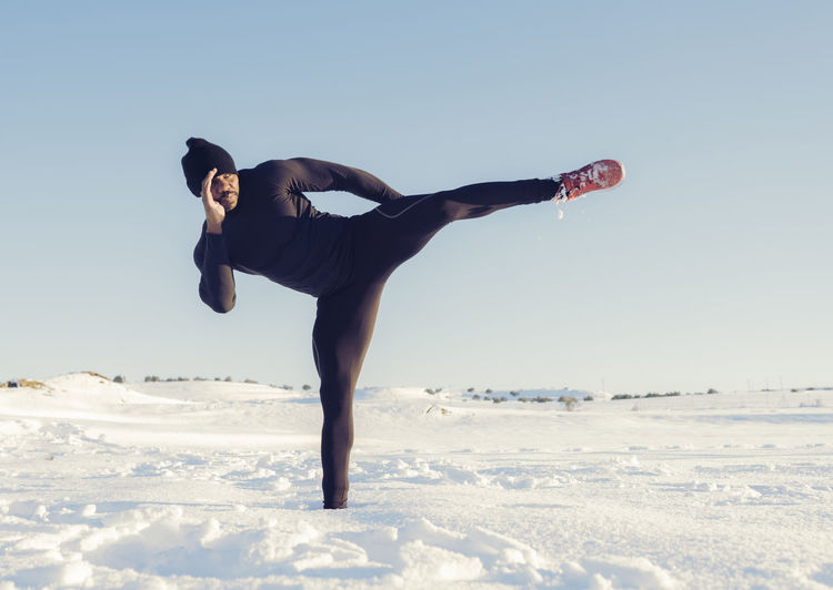 Athlete practicing kickboxing while standing in snow on sunny day
