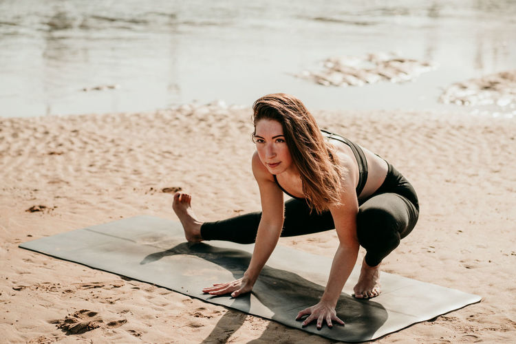 Tranquil female practicing yoga in side lunge with arms extended pose while standing looking away on mat on beach in summer