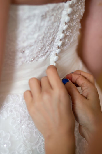Cropped hands of woman assisting bride in getting dressed