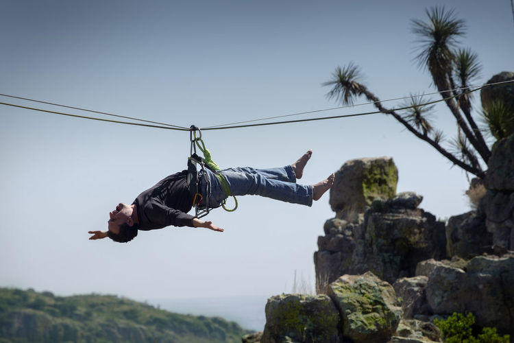 Low angle view of man hanging on zip line against sky