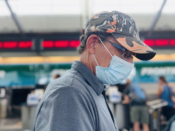 Close-up portrait of active  senior man wearing mask looking down waiting to check in at airport.  