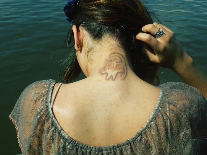 Rear view of woman showing tattoo by lake