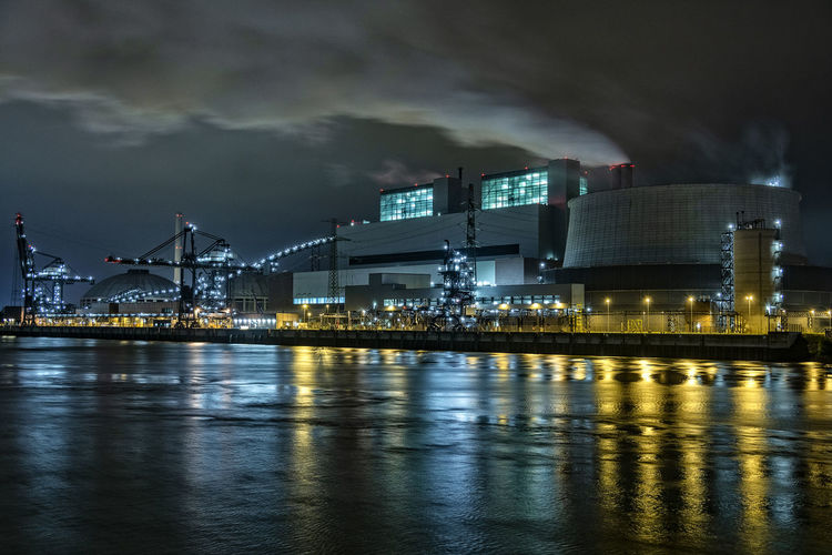 Illuminated buildings by river against sky at night