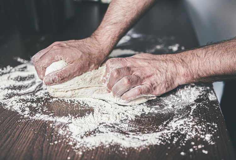 Cropped hands of mature man kneading dough on table at home