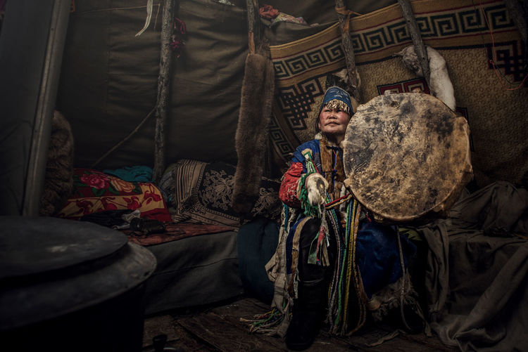Woman wearing traditional clothing holding shield in tent