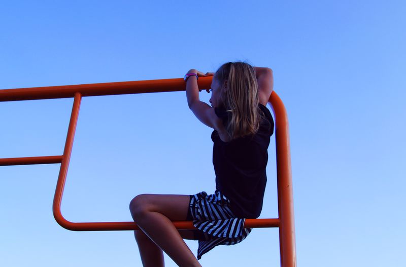 Low angle view of girl playing on railing against clear blue sky
