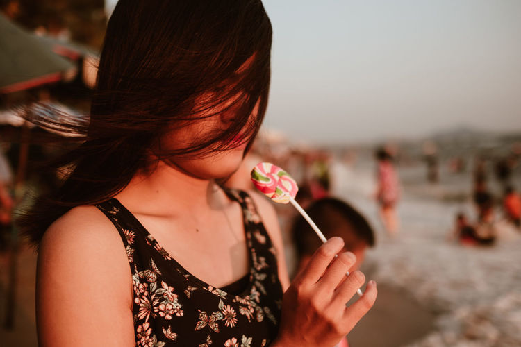 Close-up of woman with tousled hair having lollipop at beach