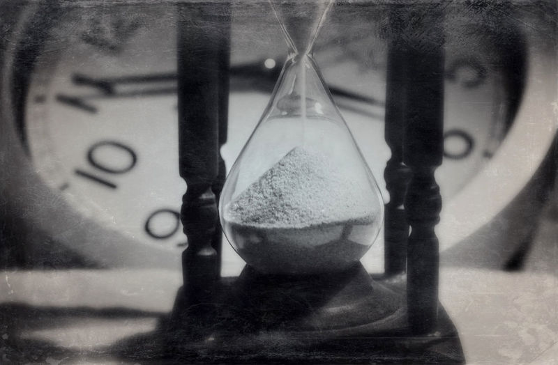 Close-up of hourglass against clock