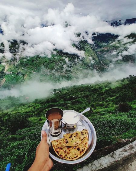 Midsection of person holding drink against mountains