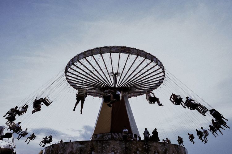 Low angle view of silhouette people sitting chain swing ride against sky