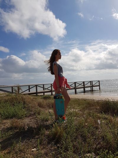 Woman holding skateboard while standing at beach against sky