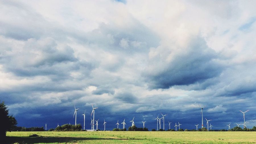 Wind turbines on field against cloudy sky