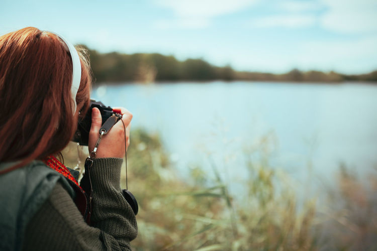 Young woman taking photos near to lake with an old analog camera
