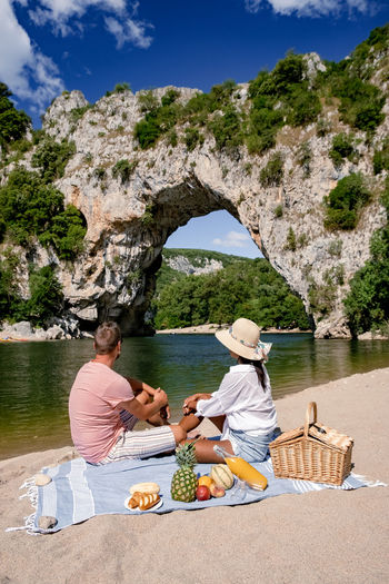 Full length of couple sitting at beach against rock formation