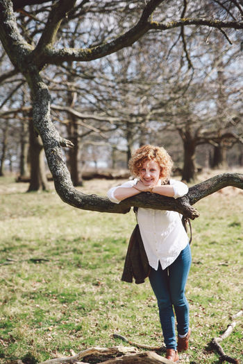 Portrait of woman standing leaning on branch at park