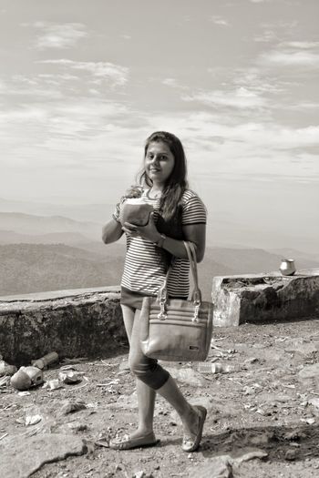 Portrait of smiling young woman drinking coconut water while standing against sky