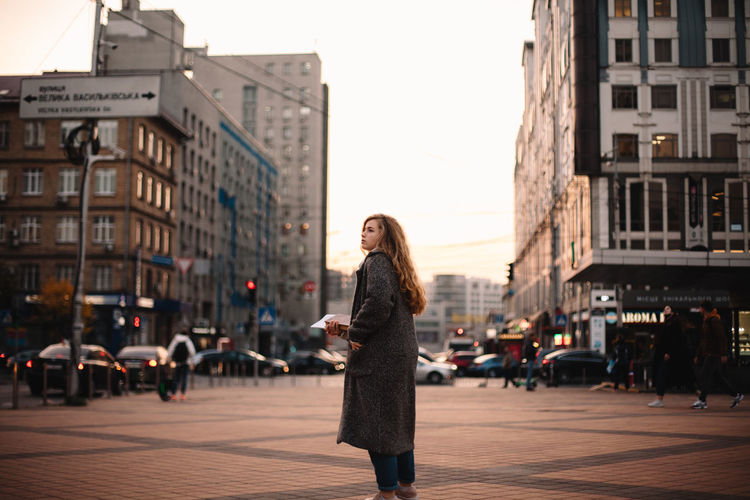 Thoughtful teenage student girl standing in city during autumn